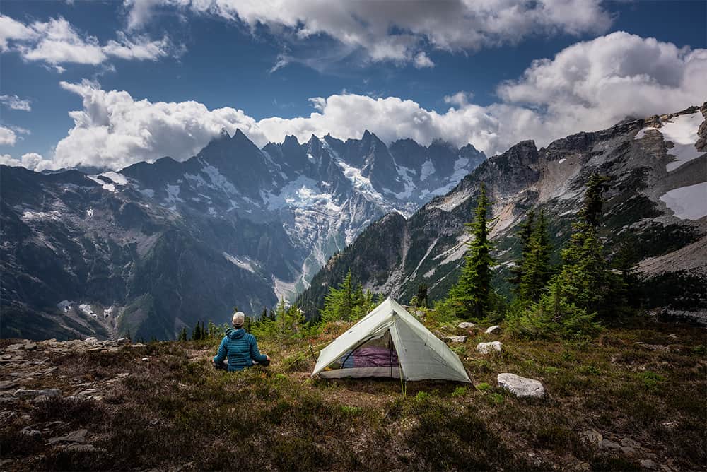 Backpacker sitting next to tent in front of mountain range