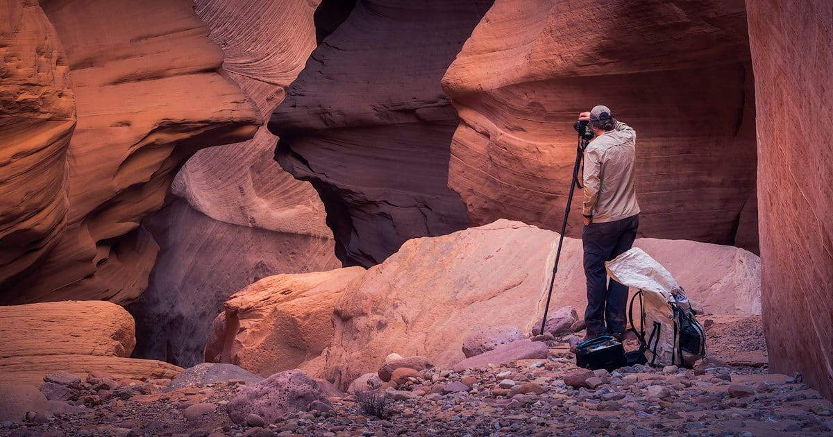 backpacker taking a photo standing next to f-stop camera case and hyperlite backpack