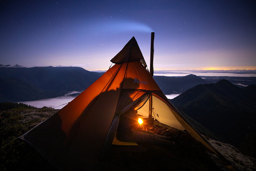 someone is siting by a wood stove in their hot tent