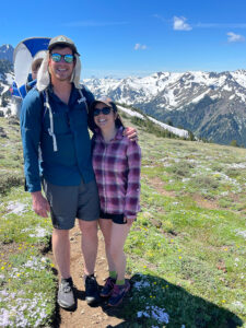 Parents hiking a mountain trail while carrying their young child in a backpack carrier during a family adventure