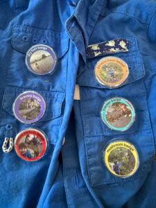 Collection of kids hiking achievement badges earned on a backpacking trip, including 10-mile hike, mushroom spotting, and tracker badges