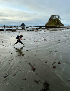 Young child jumping over a small creek on a hiking trail, building confidence and balance through outdoor play