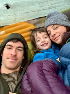 Family snuggled together inside a tent on a backpacking trip, staying cozy after a day of hiking